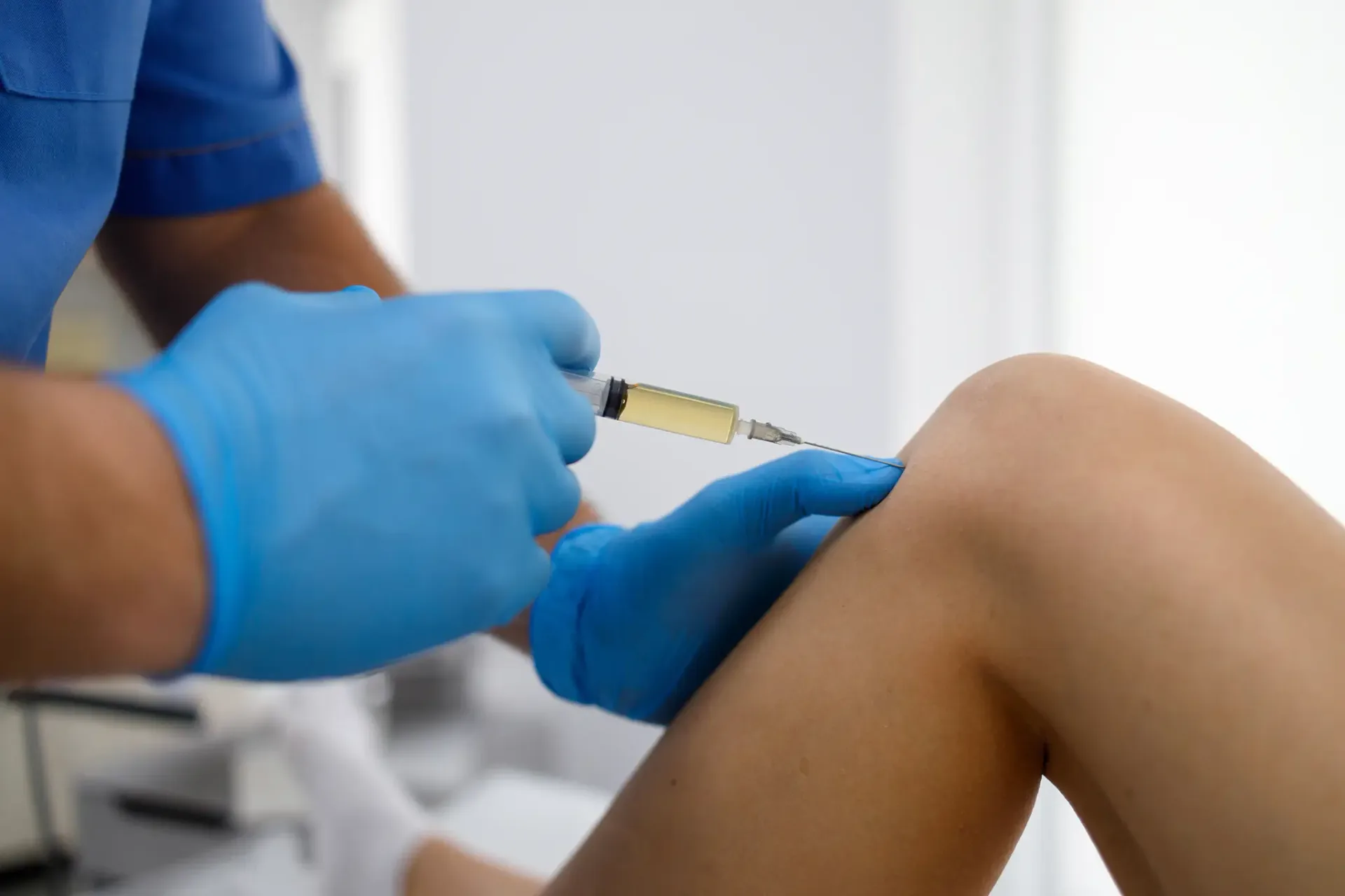 Medical professional in blue gloves administering a corticosteroid injection into a patient's knee.