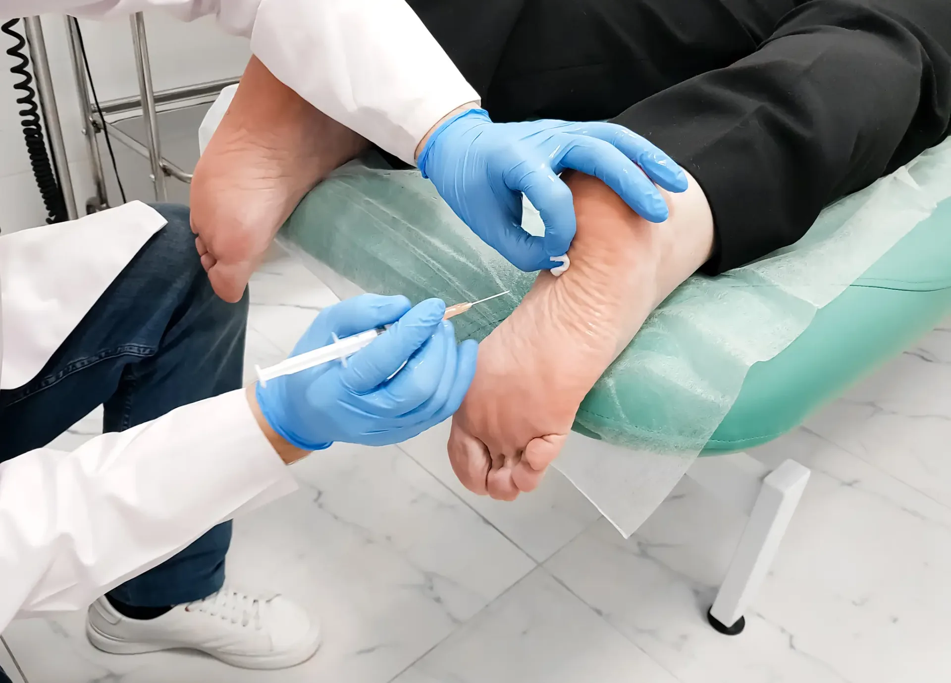 Doctor in blue gloves administering a syringe injection into a patient's foot sole.