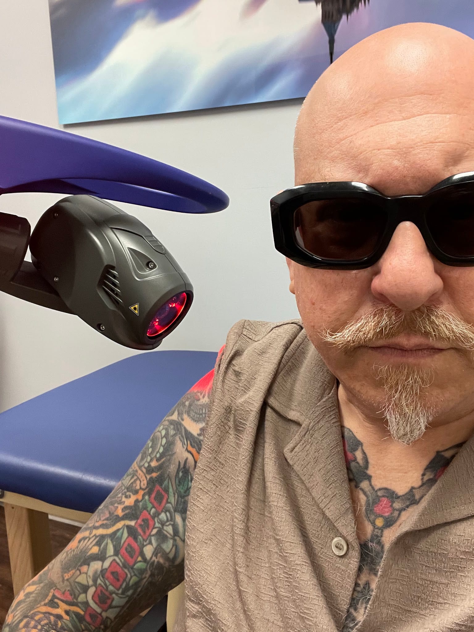 Tattooed bald man wearing protective goggles next to laser therapy device
