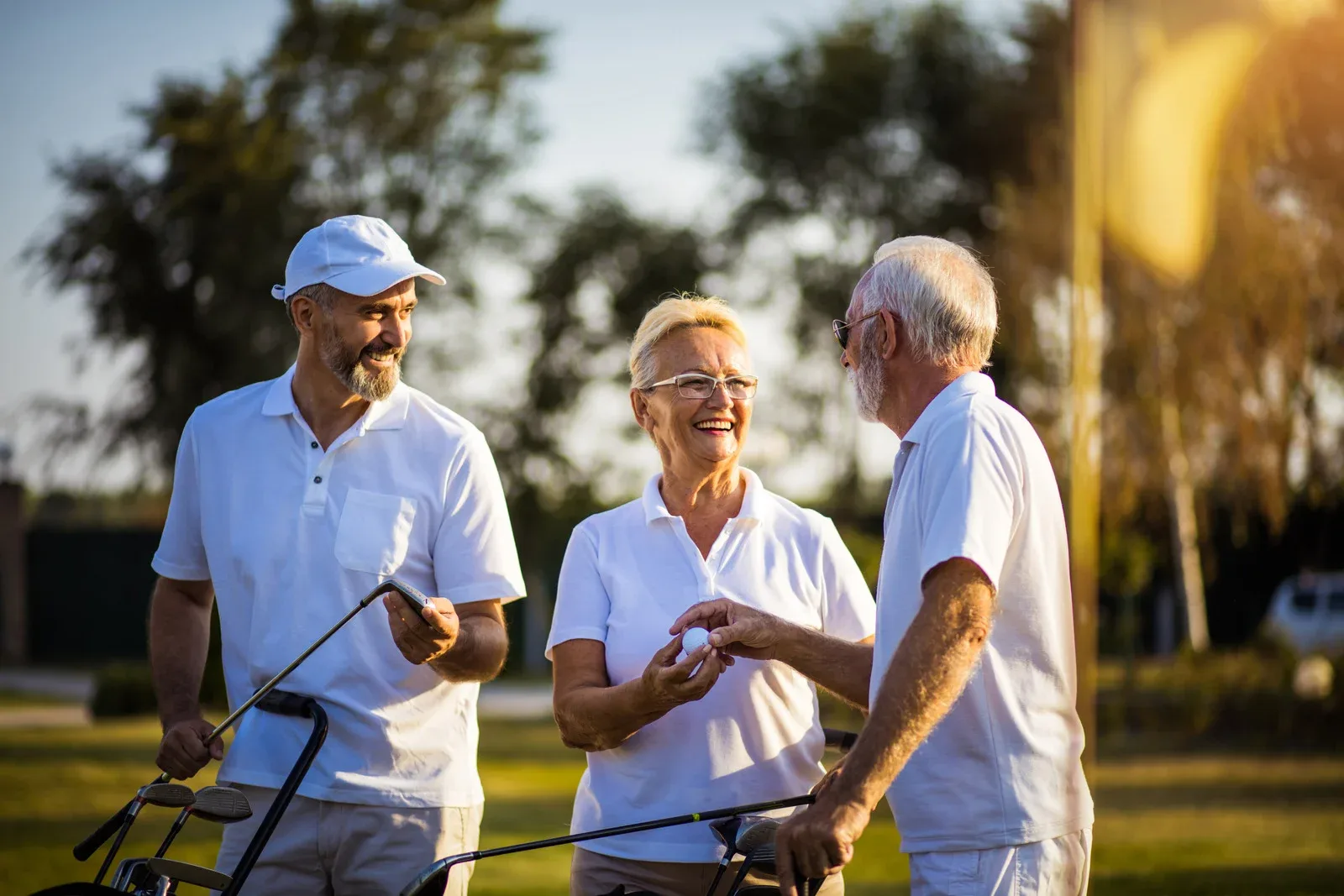 Three smiling golfers in white polo shirts chatting on a sunny course