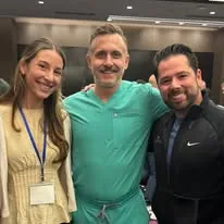 Dr. Mark Ayzenberg in scrubs posing with two colleagues at a medical event