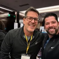 Two smiling men posing together at an indoor medical conference event