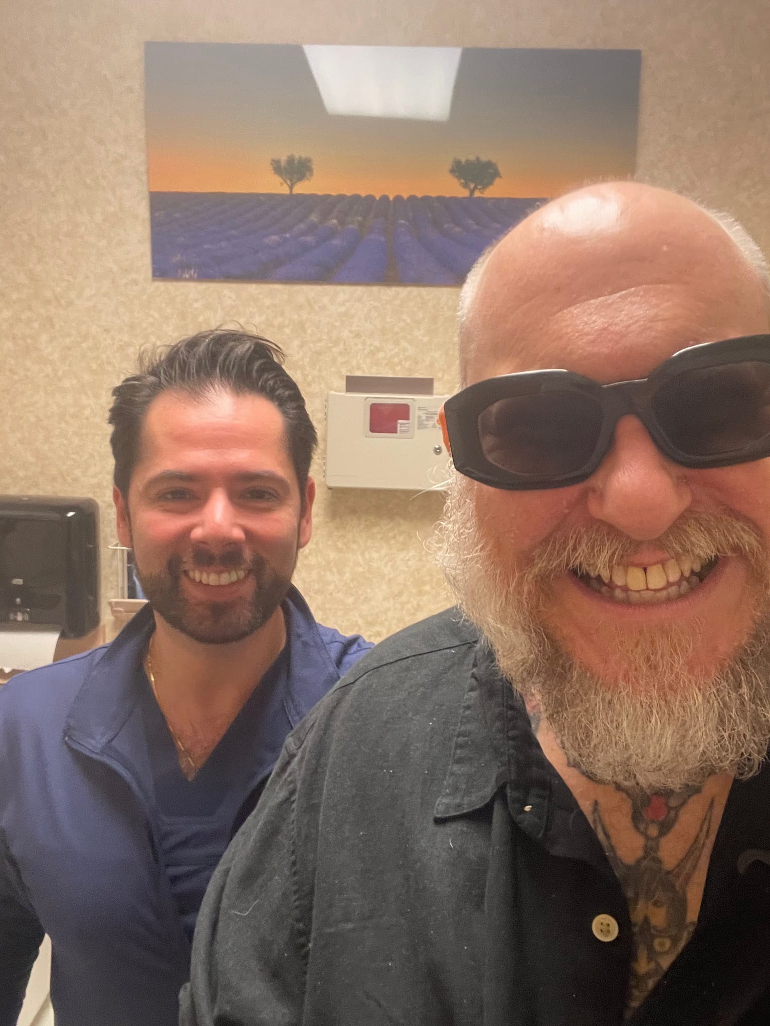 Smiling bald bearded patient with sunglasses poses with Dr. Ayzenberg in clinic
